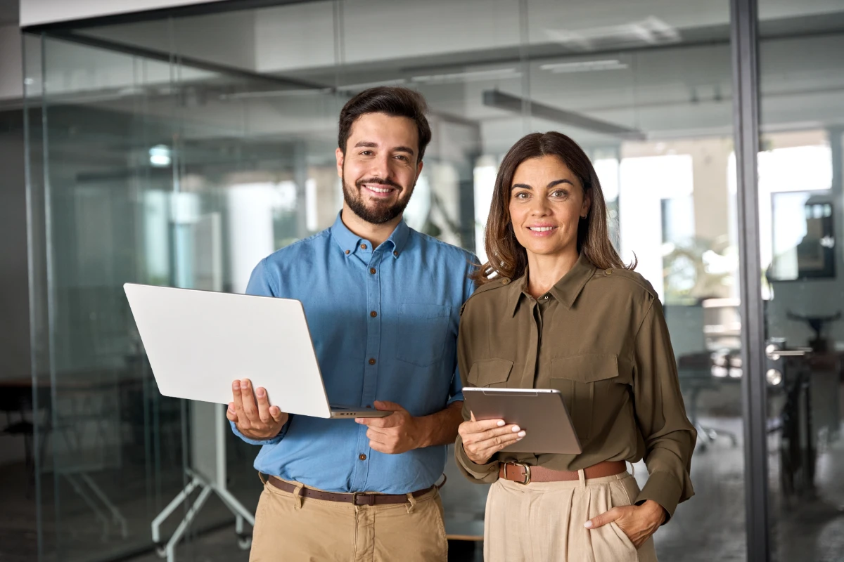 Two business partners executives standing in office looking at camera. 2 sales managers, company agents, consultancy professionals, bank advisors with devices posing for corporate portrait.