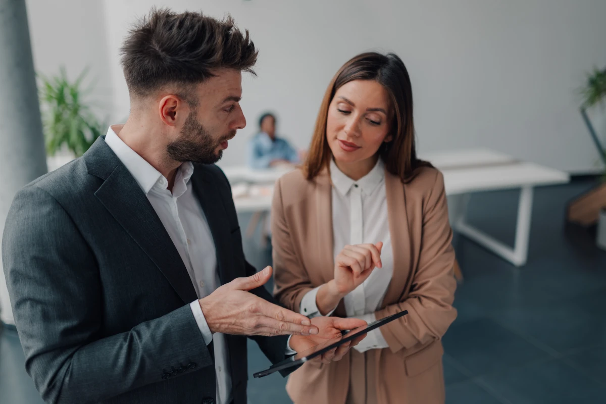 Two business colleagues collaborating in a modern office, using a digital tablet to discuss work, share ideas, and strategize on their project for effective teamwork and communication