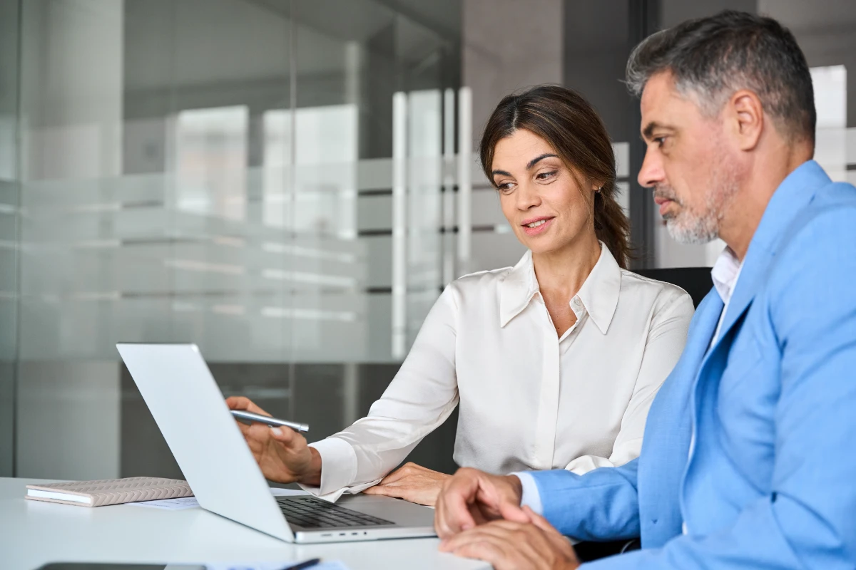 Mature business woman professional bank manager or financial advisor consulting client using laptop. Two older executives team business people man and woman working at office corporate meeting.