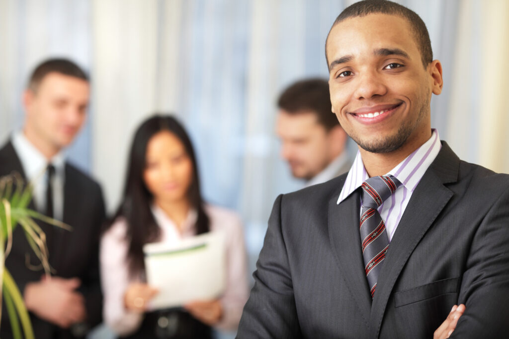 Young corporate professional standing confidently with his colleagues in the background.